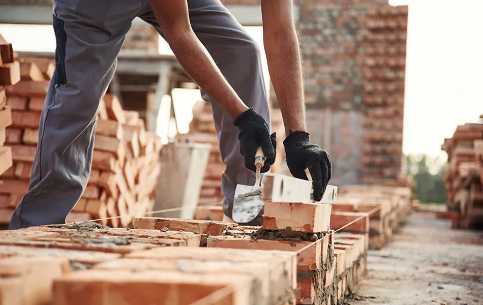 Un hombre con guantes coloca ladrillos para construir un muro