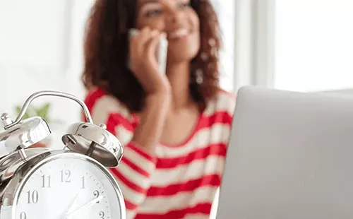 Primer plano de un reloj y empleada trabajando, ilustración de la nueva ley de control horario 2025