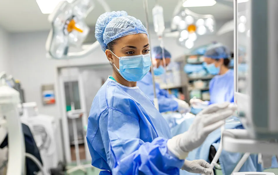 Un médico, vestido con bata quirúrgica y mascarilla protectora, prepara el equipo de anestesia